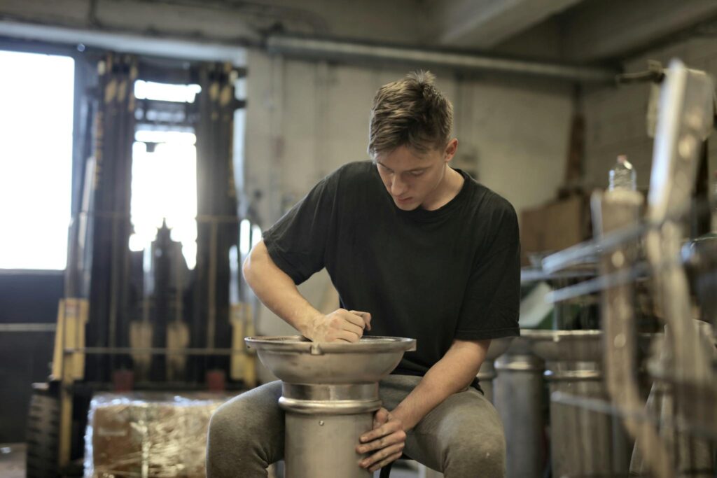 Focused young man working on metal craftsmanship in an industrial workshop setting.