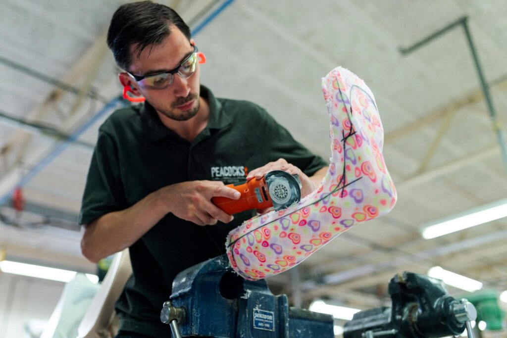 Orthotic technician using power tool to craft a colorful ankle foot orthosis in a workshop.